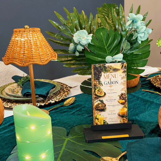 Black Bon Appétit menu holder with a gold plaque displaying the Gabon menu among tropical greenery