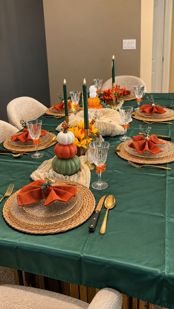 Evergreen Thanksgiving table with green linen, woven placemats, orange napkins and autumn centerpieces