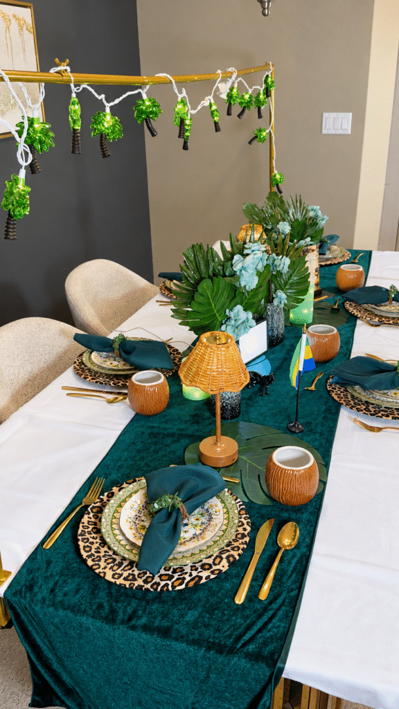 Gabon dinner table with a white tablecloth, deep teal runner, tropical foliage, leopard-print chargers and gold cutlery