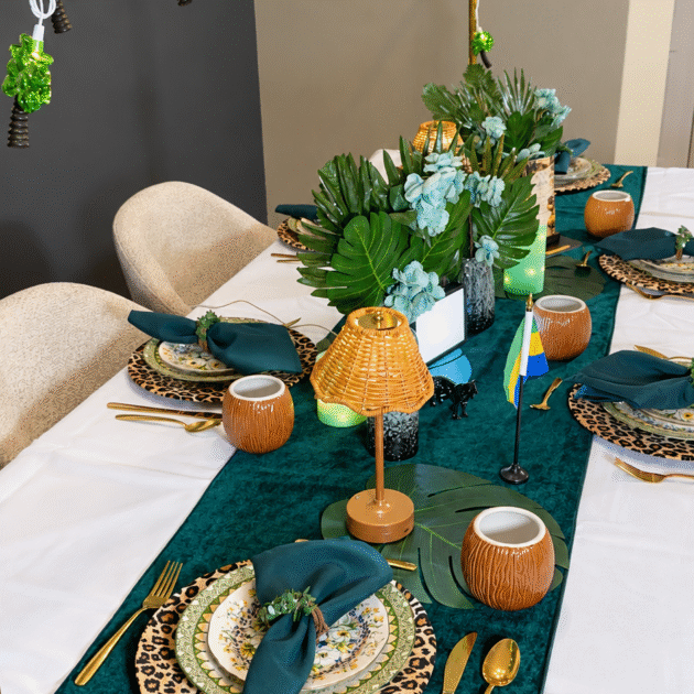 Gabon dinner table with a white tablecloth, deep teal runner, tropical foliage, leopard-print chargers and gold cutlery