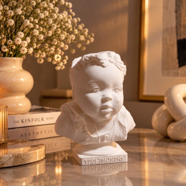 White portrait statue with a bow and personalized base, displayed beside a candle and flowers